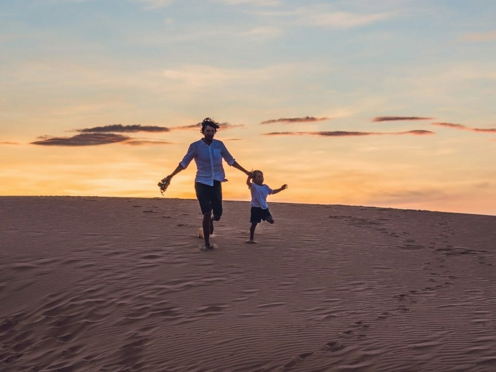 Father and child running down dune, Namibia