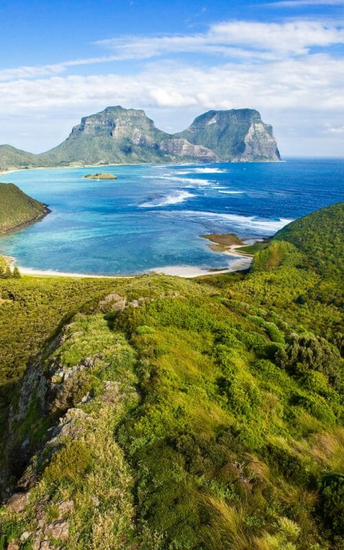 Panoramic view across the length of Lord Howe Island with greenery in foreground to Mount Gower in distance.